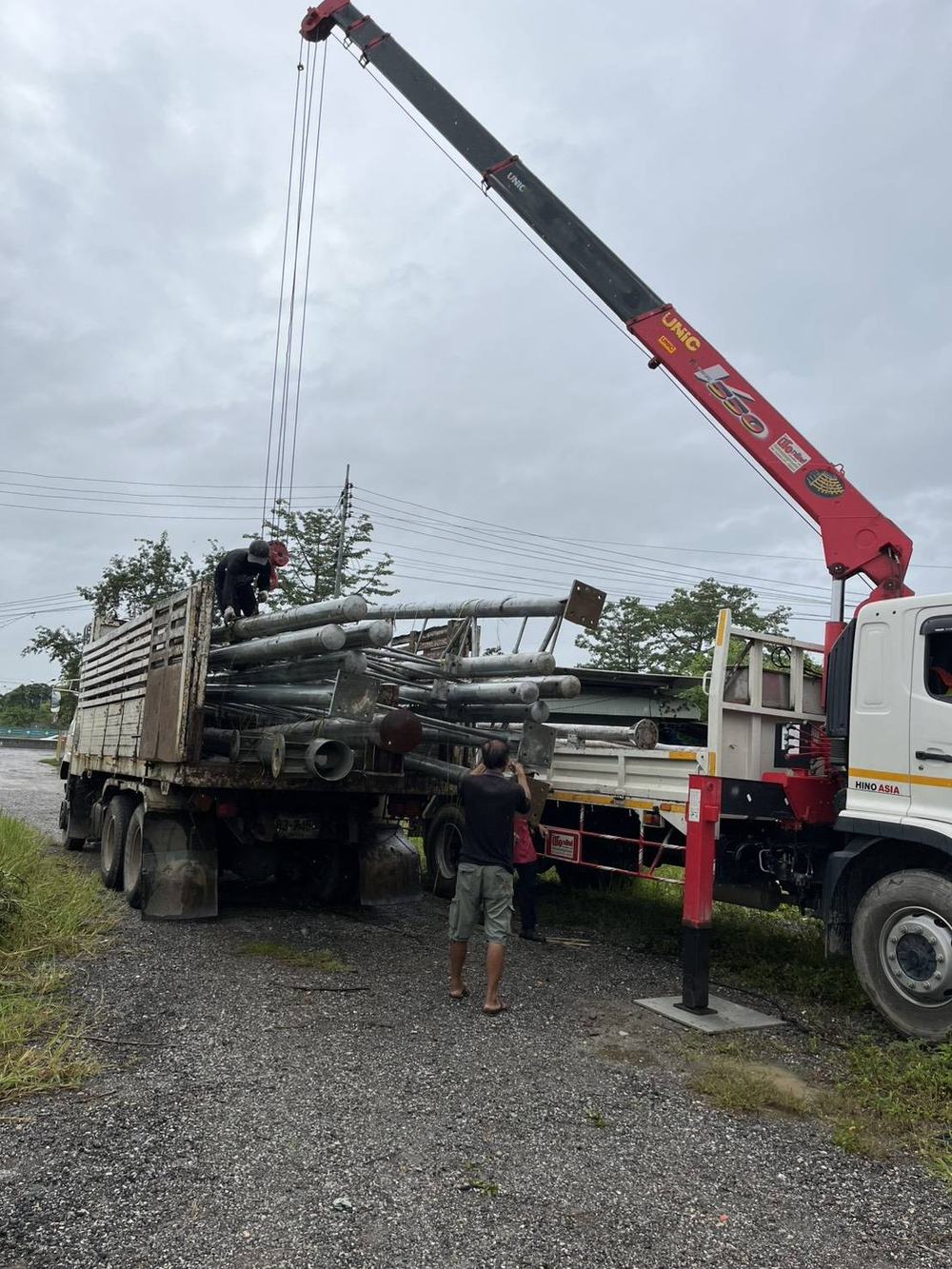 ทีมงานใช้รถเครนยกเสาเหล็กขึ้นรถบรรทุก